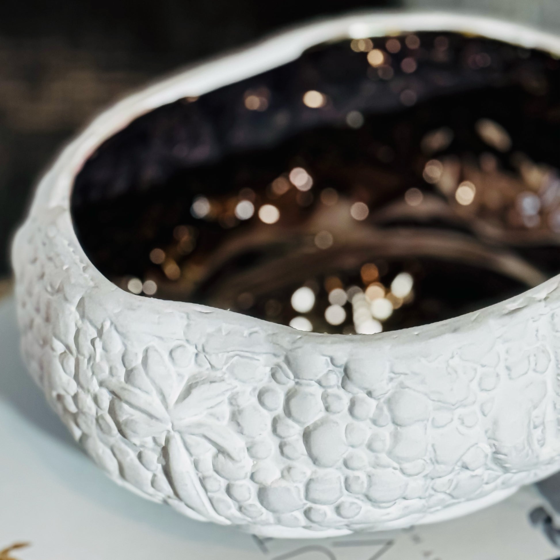 A white ceramic decorative bowl with a floral pattern and a reflective surface.