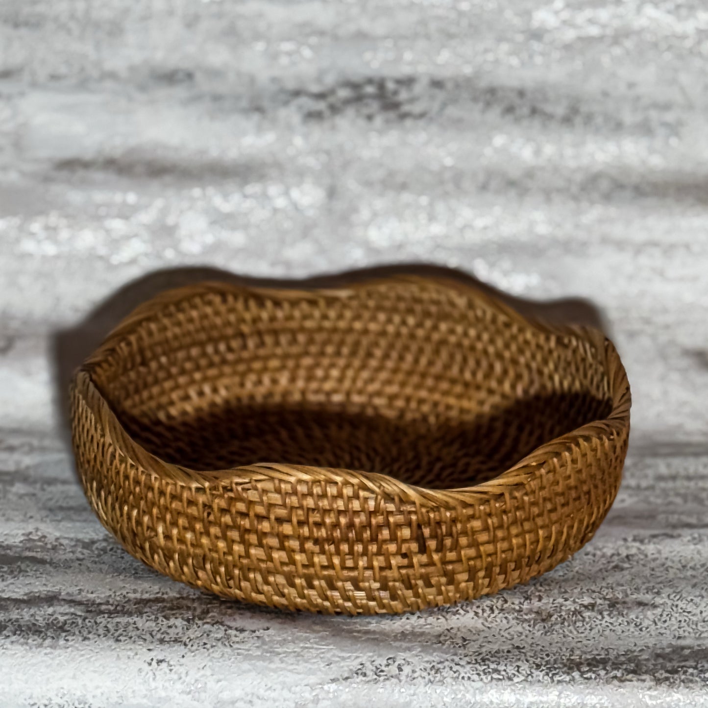 A round, brown rattan basket with a timeless design, handmade from rattan, displayed against a grey background.